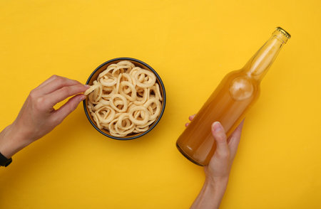 Female hands hold beer and snacks corn rings on yellow backgroundの写真素材