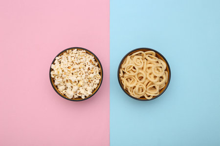 Bowls of snacks (popcorn and corn rings) on a blue-pink background. top viewの写真素材