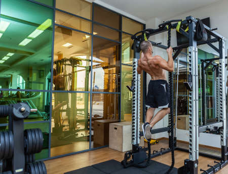 muscular man with a naked torso pulls up on the ropes in the gym