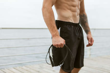 Embossed muscular man holding skipping rope on the beach