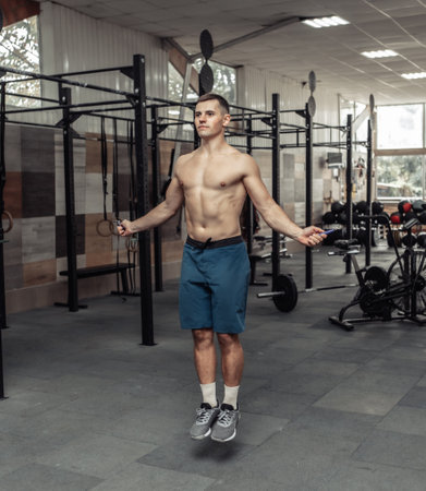 Muscular sport man with a naked torso jumps on a skipping rope in a modern cross gym. Cartio...