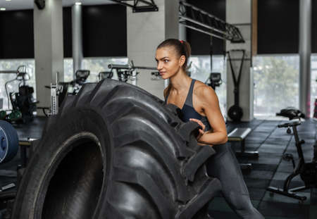 Young cross fit woman pushing heavy big wheel in modern gym. functional training. healthy lifestyleの写真素材