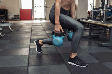 Young muscular woman in sportswear trains lunges with a kettlebells in the gym. Healthy lifestyle concept. functional trainingの写真素材