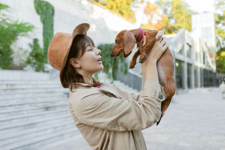 Portrait of a young fashion woman and a lovely dachshund puppy in a city park. Mistress and petの写真素材