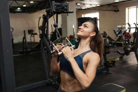 Athletic woman muscular exercising her back in lat exercise machine with narrow grip in the gym
