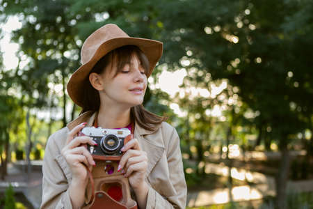 Portrait of young fashion woman in felt hat with retro camera in city parkの写真素材