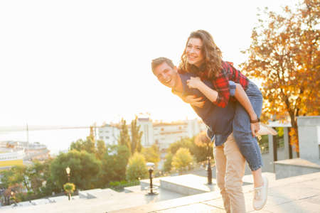 Young couple having fun in the city at sunrise. Handsome man giving his girlfriend piggy back ride. Enjoying every moment together.の写真素材