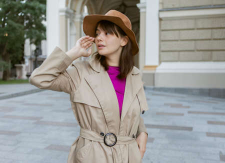Fashion portrait of young woman in a felt hat and autumn trench coat in cityの写真素材