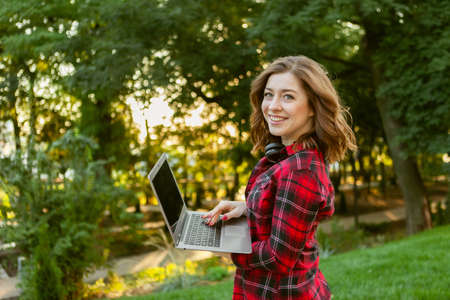Young smiling woman with tuden with laptop in parkの写真素材