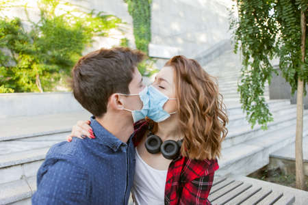 Young Couple in love, man and woman kissing each other in protective medical mask on face outdiir....