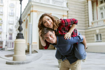 Young couple having fun outdoors. Handsome man giving his girlfriend piggy back ride. Enjoying every moment together.の写真素材