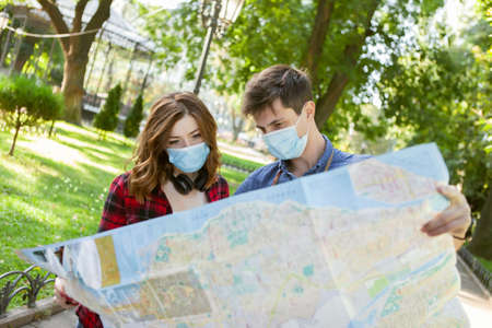 Traveling in the period. Young couple of tourists in medical protective masks exploring the city map...