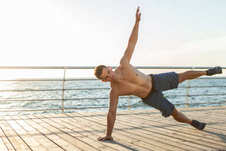 Young muscular man practicing yoga asana at sunrise on the beach