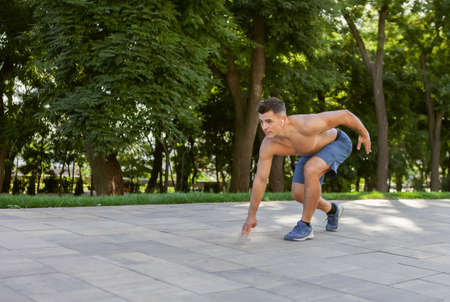 Muscular man with naked torso ready to run at sunrise in park