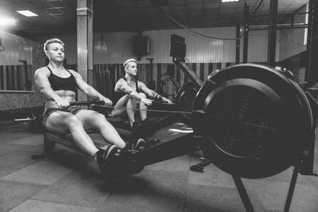Muscular sporty women workout on training simulator in crossfit gym. Sportswomen exercising on...