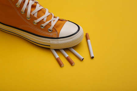 Gumshoe sneaker stepped on cigarettes on yellow background. Quitting smoking conceptの写真素材