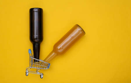 Mini shopping cart with bottles of beer on yellow background. top view
