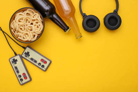 entertainment time. Gamepads and snack bowl, beer bottles, headphones on yellow background. top...