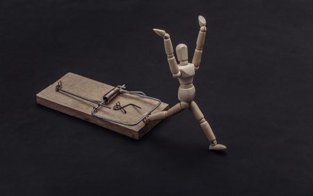 Wooden puppet caught by a mousetrap on a black backgroundの写真素材