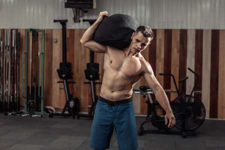 Muscular male athlete exercising with heavy bag in modern cross gym. functional trainingの写真素材
