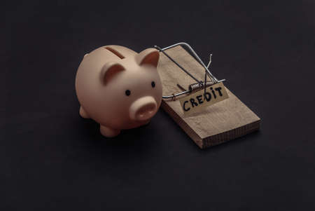 Mousetrap with loan bait and piggy bank on black background. Traps, risks or deception concept