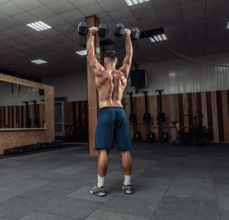 Powerful athletic man training shoulder muscles with heavy dumbbells doing overhead in gym. healthy lifestyle conceptの写真素材