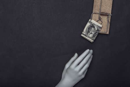 Hand reaches for mousetrap with one hundred dollar bills on black backgroundの写真素材