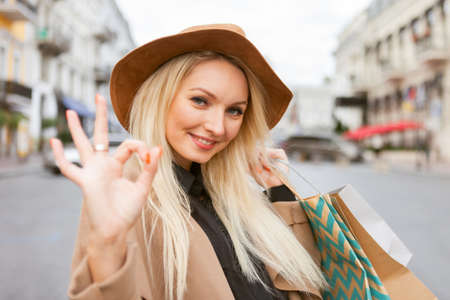 Cute attractive shopaholic woman in autumn coat and hat holding many paper shopping bags in the cityの写真素材