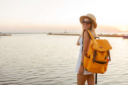 Portrait of a young woman tourist with a large travel backpack at sunrise at sea. Travel and tourism conceptの写真素材