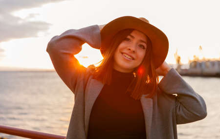 Stylish woman in felt hat and coat at sunrise at seaの写真素材