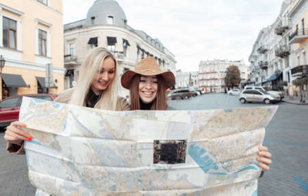 Two smiling girlfriends of tourist in autumn clothes hold map of the city and orientate in unfamiliar European city. Travel and tourism conceptの写真素材
