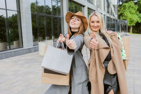 Two women shopaholic friend in autumn clothes are holding many shopping bags and walking around the city. Lifestyle, leisure conceptの写真素材