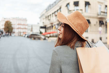 Cute attractive shopaholic funny woman in autumn coat and hat holding many paper shopping bags iin European cityの写真素材
