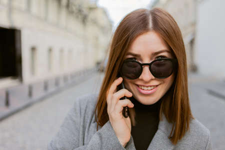 Portrait of a cute woman with straight hair and sunglasses talking on the phone in the city