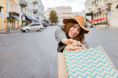 Attractive funny shopaholic woman in autumn coat and hat holding many paper shopping bags iin European cityの写真素材
