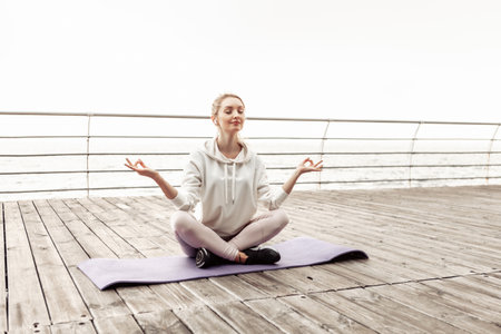 Healthy and relaxed young fit woman meditating while sitting on mat on the beachの写真素材