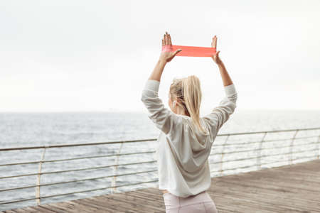 Young fit woman exercises hands with fitness rubber bands on the beach. healthy lifestyleの写真素材
