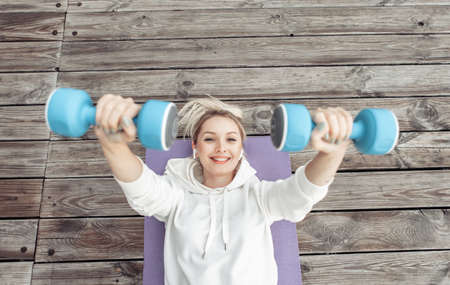 Young fitness woman practicing lying dumbbell press on mat outdoors. healthy lifestyleの写真素材