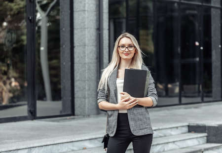 Happy young blonde business woman with folder at office buildingの写真素材