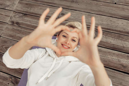 Young cheerful fit woman shows fingers in the shape of a heart while lying on the mat. healthy lifestyle. sports lover. top viewの写真素材