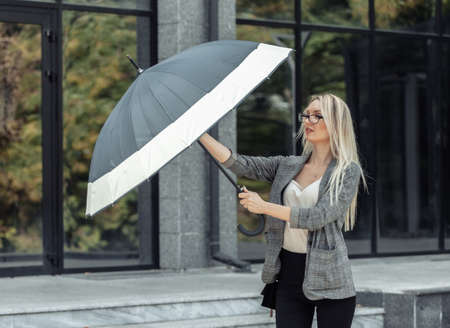Blond business woman with umbrella on the background of a business office. waiting for the rainの写真素材