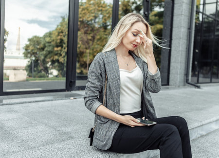 Business woman tired of work, sitting outdoors on the stairs, working life, burnout syndrome from office work. Headache, nervous tensionの写真素材