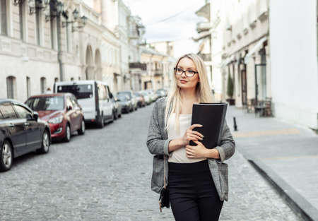 Portrait of confident business woman with folder in hands in urban streetの写真素材