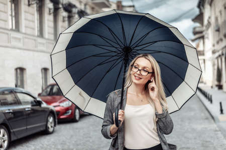 Blond business woman with umbrella in urban street. waiting for the rainの写真素材