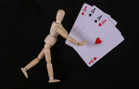 Wooden puppet mannequin holding four aces isolated on black backgroundの写真素材