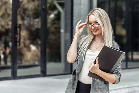 Happy young blonde business woman with folder at office buildingの写真素材