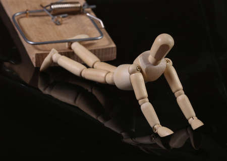 Wodden Puppet caught in a mousetrap on black background