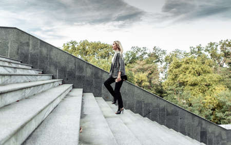 Purposeful, self-confident business lady climbs the stairs outdoors in cloudy weather. career growth conceptの写真素材