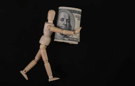 Wooden puppet mannequin holding one hundred dollar bills isolated on black background