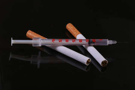 Cigarette and syringe isolated on black background. Nicotine and drug addictionの写真素材